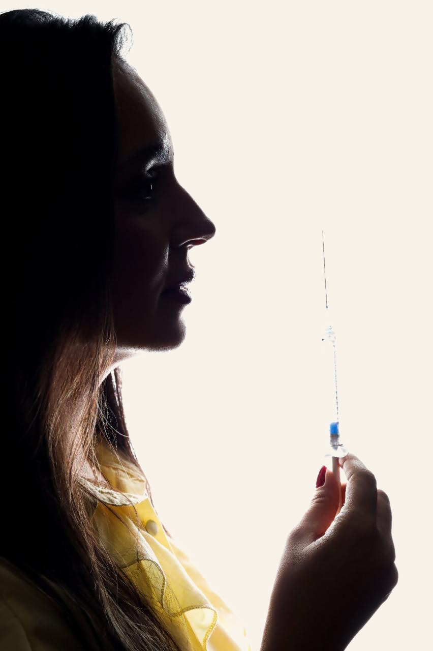 Silhueta da Dra. Michely Carvalho em contraluz segurando uma seringa
